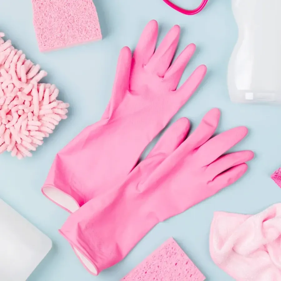 A pair of pink cleaning gloves with sponges and cloths on a light blue surface