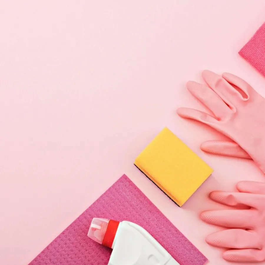 Yellow sponge, pink gloves, pink cloth, and a cleaner bottle on a pink background
